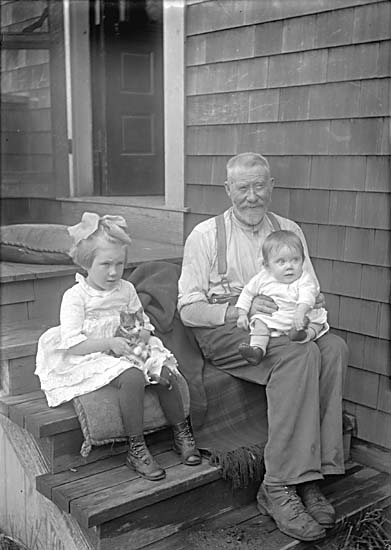 Man sitting on steps with a baby and young girl with kitten sitting beside him
